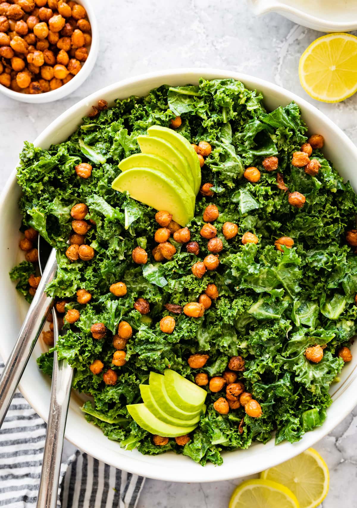 Kale salad topped with crispy roasted chickpeas and avocado slices in a white serving bowl.