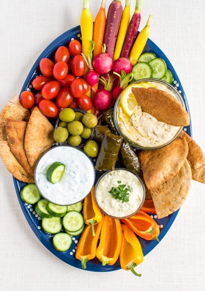 Vegetarian mezze platter with carrots, radishes, tomatoes, cucumber slices, green olives, domades, pita chips, peppers and a variety of hummus and dips.