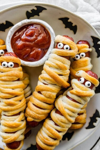Mummy hot dogs on a Halloween plate served with ketchup for dipping.