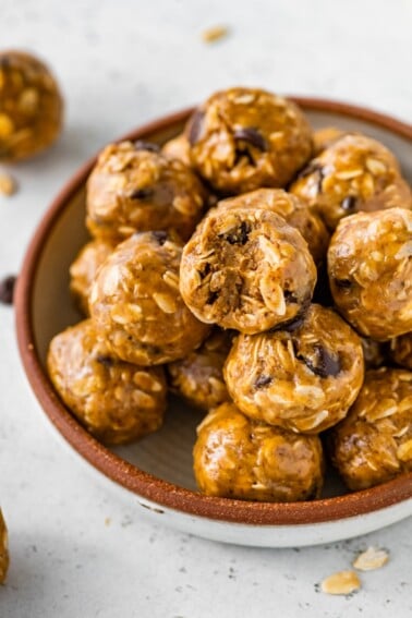 No bake energy balls piled in a bowl, with one ball showing a bite taken out of it.