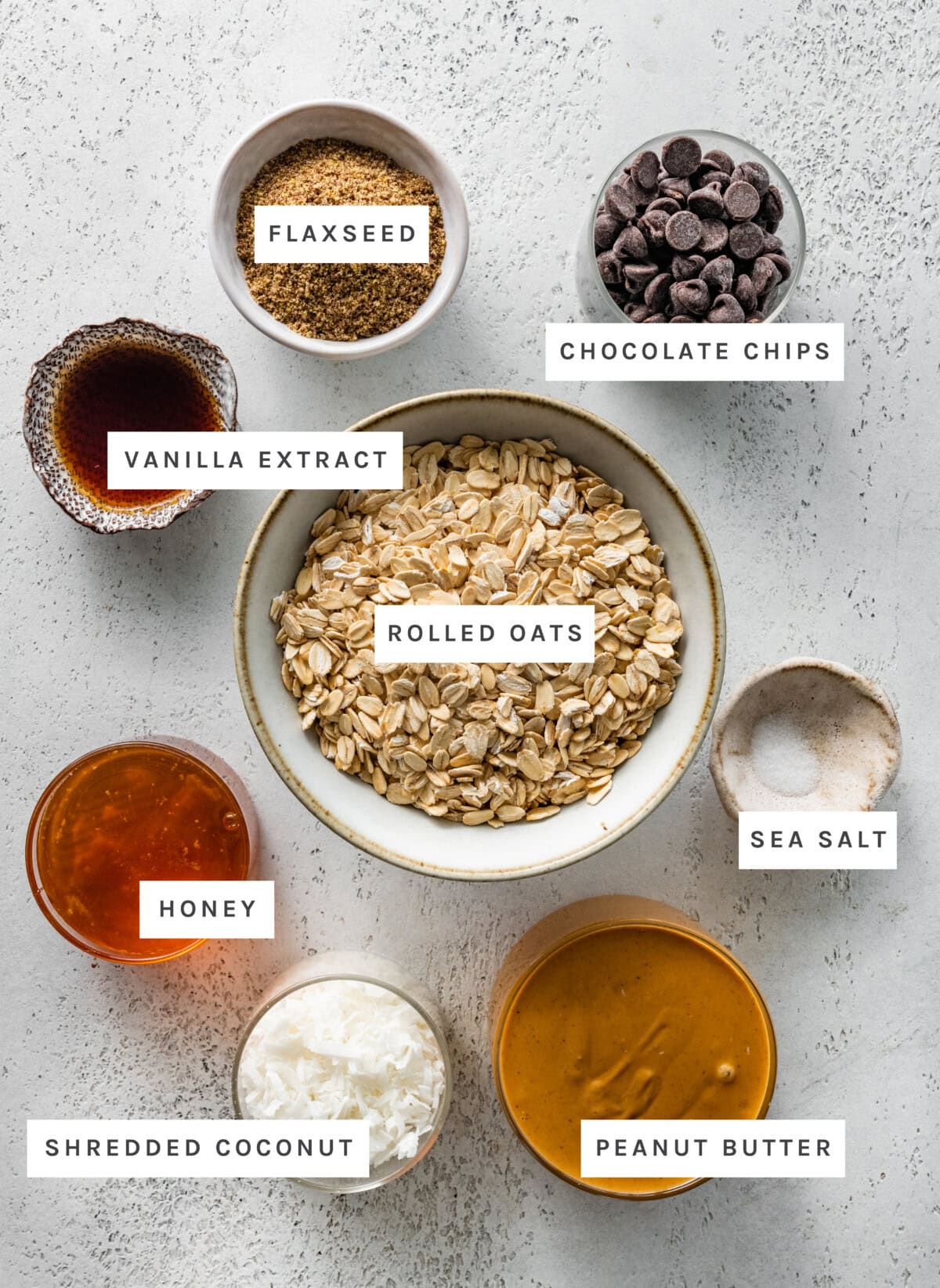 Ingredients measured out to make No Bake Energy Balls. Vanilla Extract, Honey, Shredded Coconut, Peanut Butter, Sea Salt, Chocolate Chips, Flaxseed and Rolled Oats.