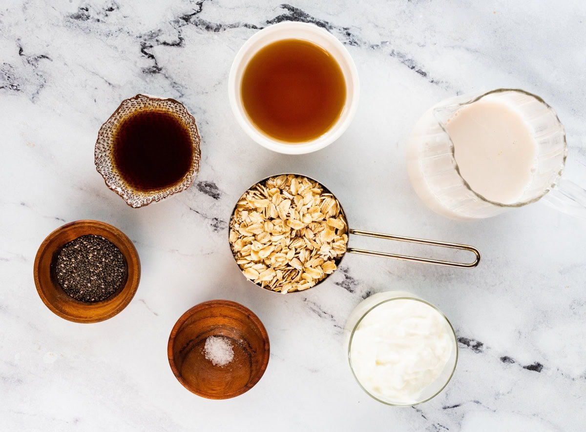 Ingredients measured out to make overnight oats: almond milk, Greek yogurt, maple syrup, oats, sea salt, vanilla and chia seeds.