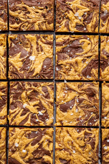 Peanut butter brownies cut into 16 squares. The brownies are topped with a peanut butter swirl and flaked sea salt.