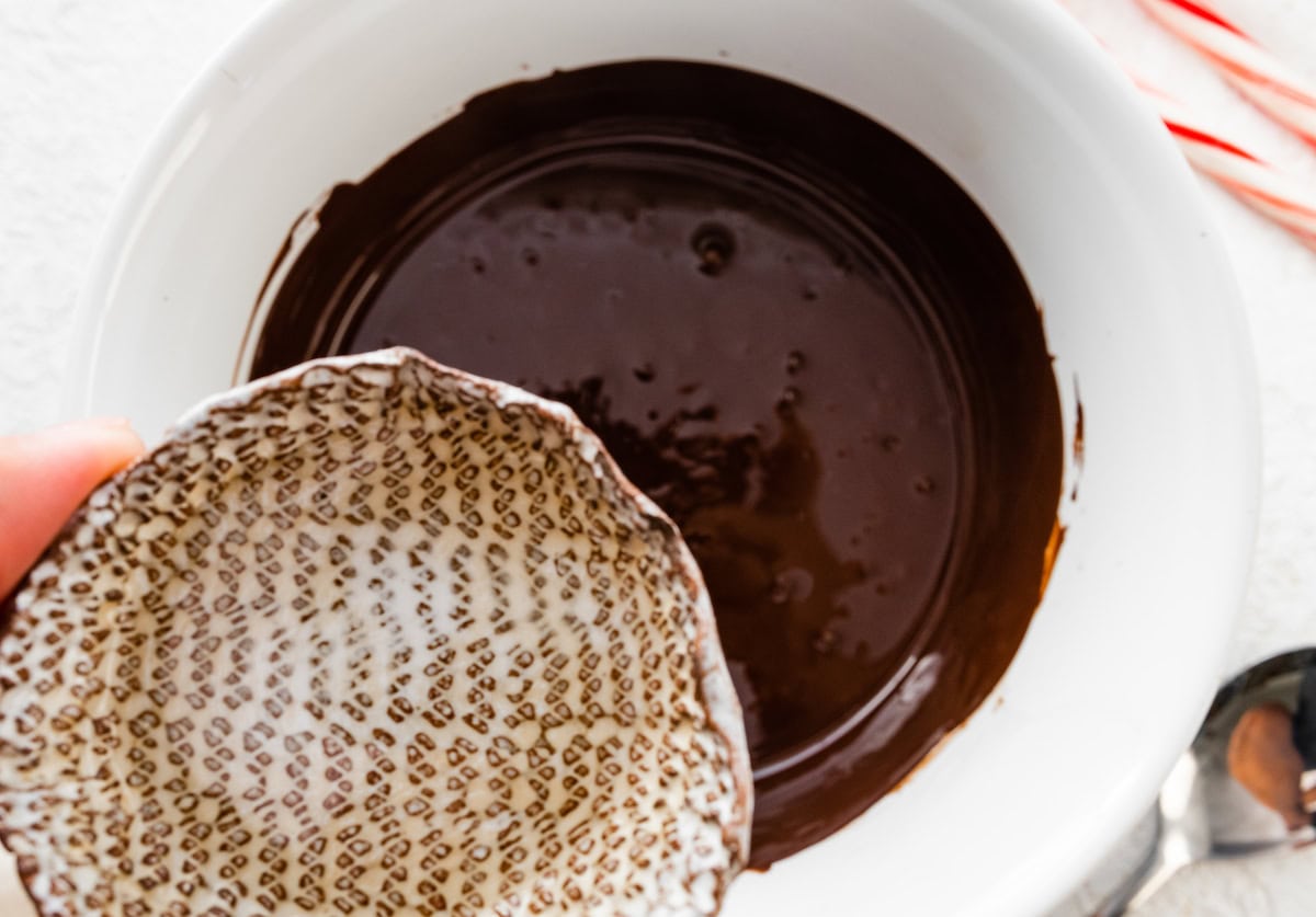 A woman's hand pouring peppermint extract into melted dark chocolate.