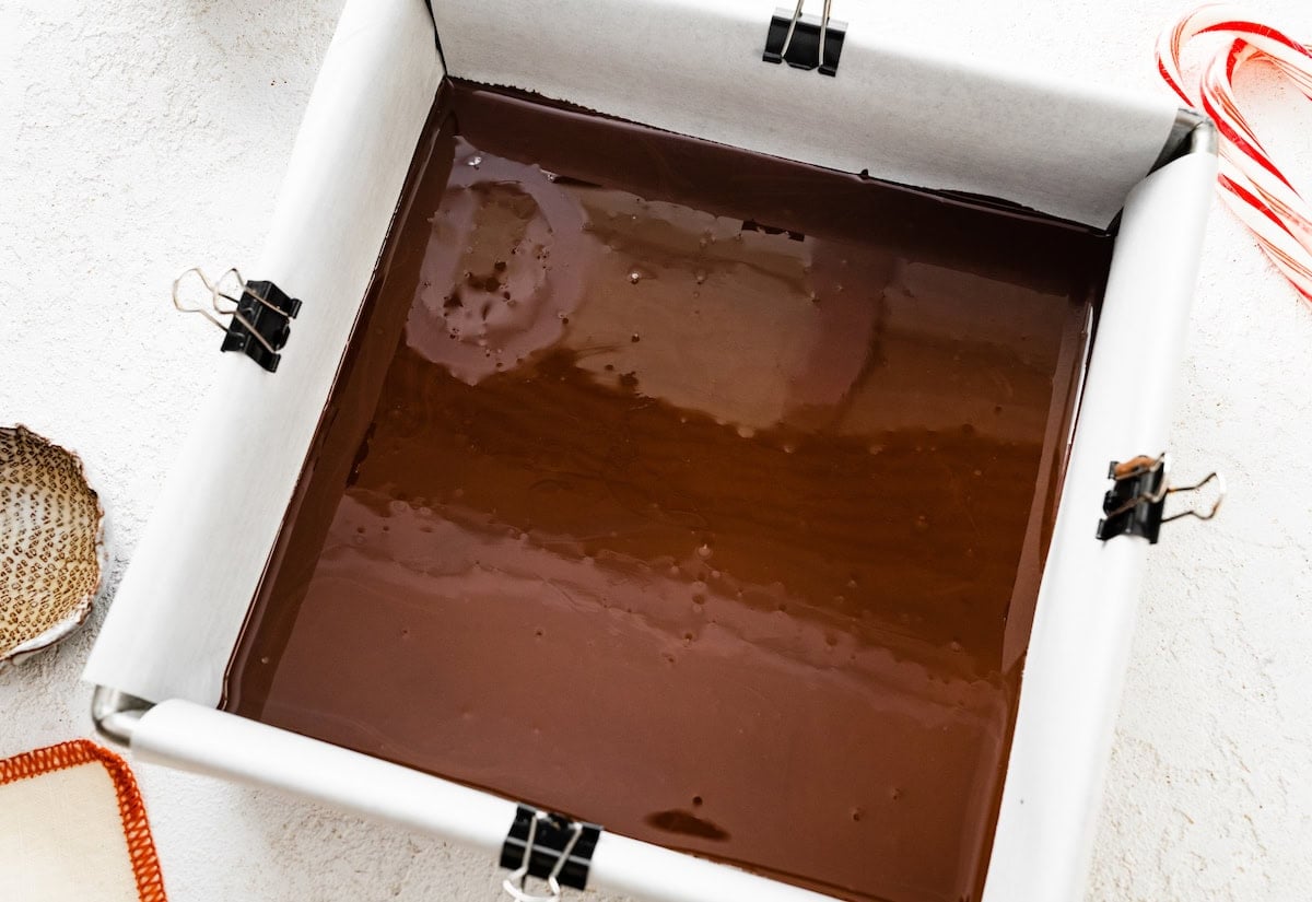 A layer of melted dark chocolate in the bottom of a 8x square baking dish that's lined with parchment paper.