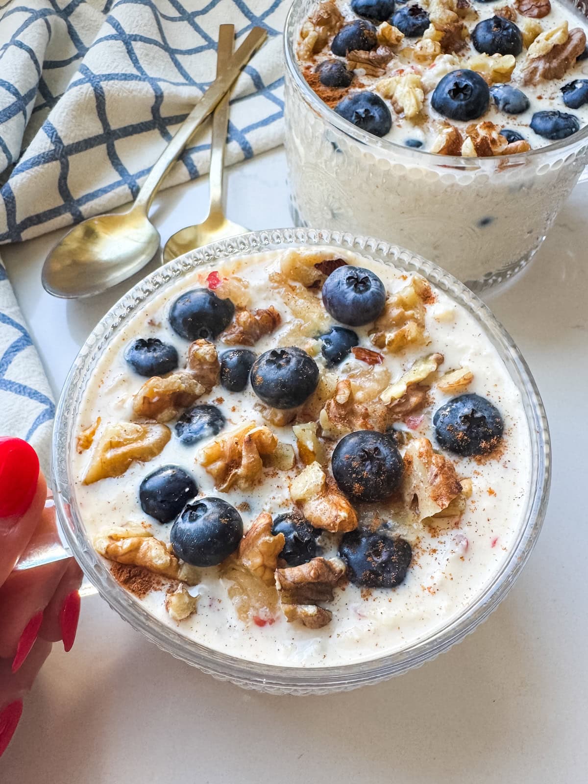 Overnight oats in a glass bowl, garnished with blueberries and walnuts, with a gold spoon and another bowl in the background.