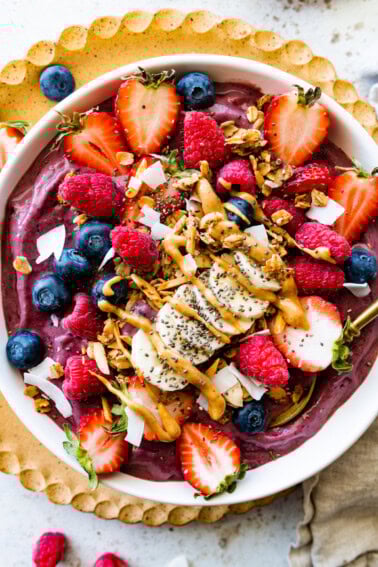 A protein acai bowl topped with fresh berries, banana slices, chia seeds, coconut shreds, and a drizzle of almond butter.