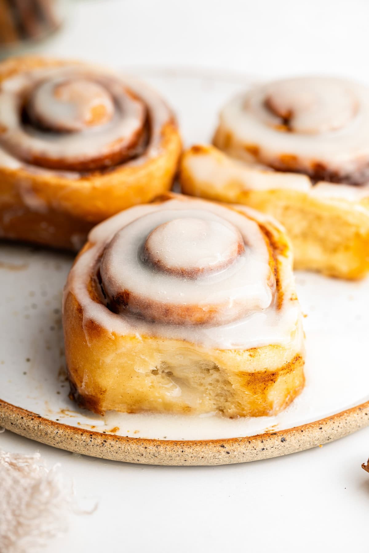 A white plate with three protein cinnamon rolls, each topped with a white glaze.