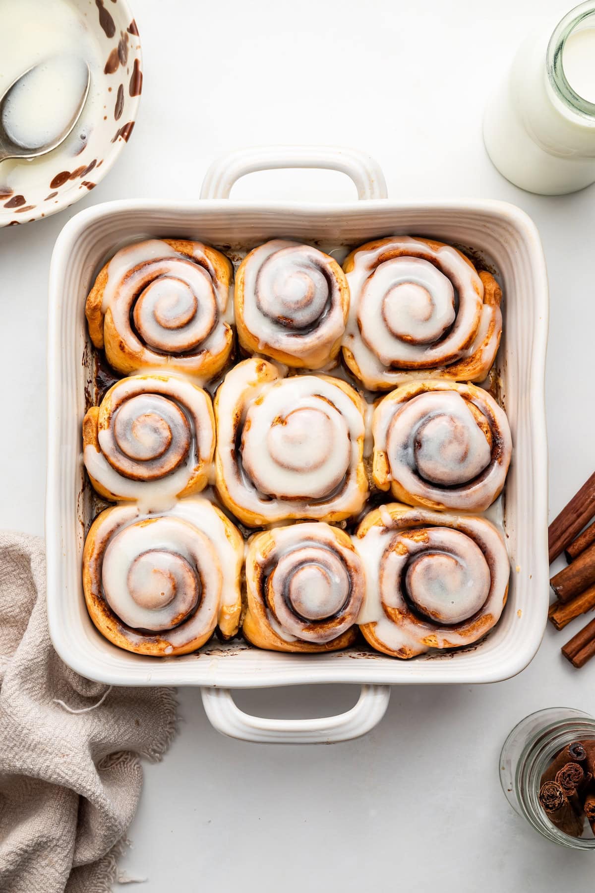 A white square baking dish filled with baked cinnamon rolls that are topped with a glaze.