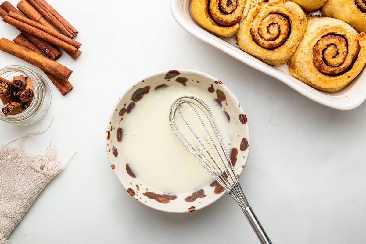 The icing for the protein cinnamon rolls mixed together in a shallow dish with a silver whisk.