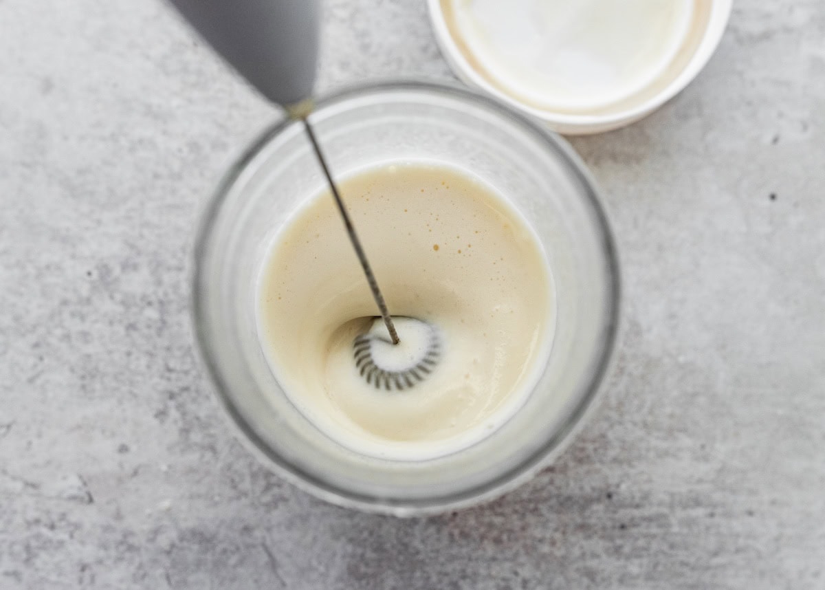 Frothing milk and vanilla protein powder in a small cup to make protein cold foam.