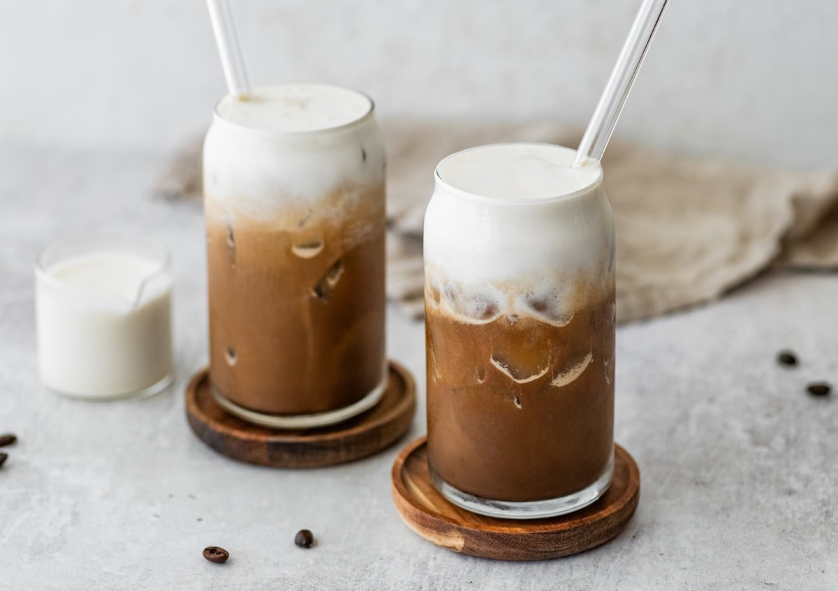 Iced coffee topped with creamy protein cold foam in tall glasses with glass straws.