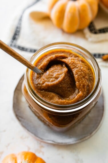 A glass jar full of pumpkin butter with a spoon inside.