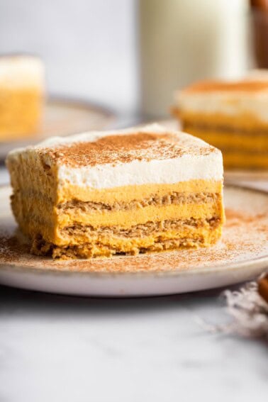 A slice of pumpkin icebox cake on a plate sprinkled with cinnamon, with additional slices in the background.