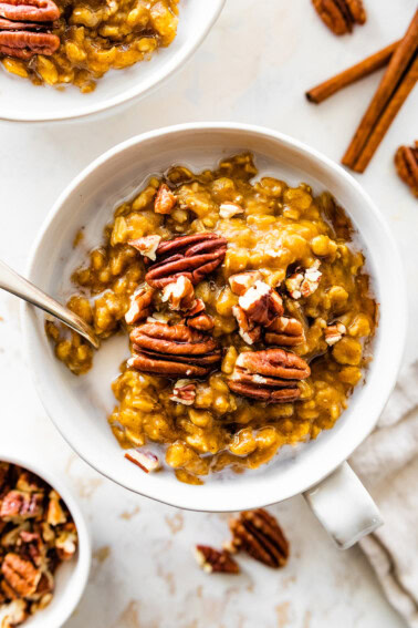 A bowl of pumpkin oatmeal with milk, and topped with pecans.