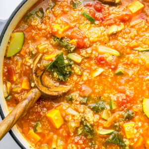 A large pot of vegetable packed quinoa soup with a wooden serving spoon in the soup.