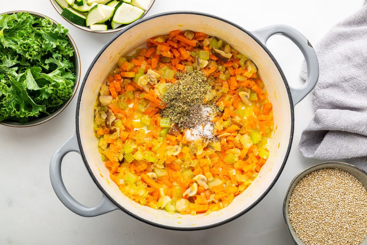 A large pot of multiple sauteed vegetables including onion, carrot, celery, and mushrooms. Along with dried herbs and spices.
