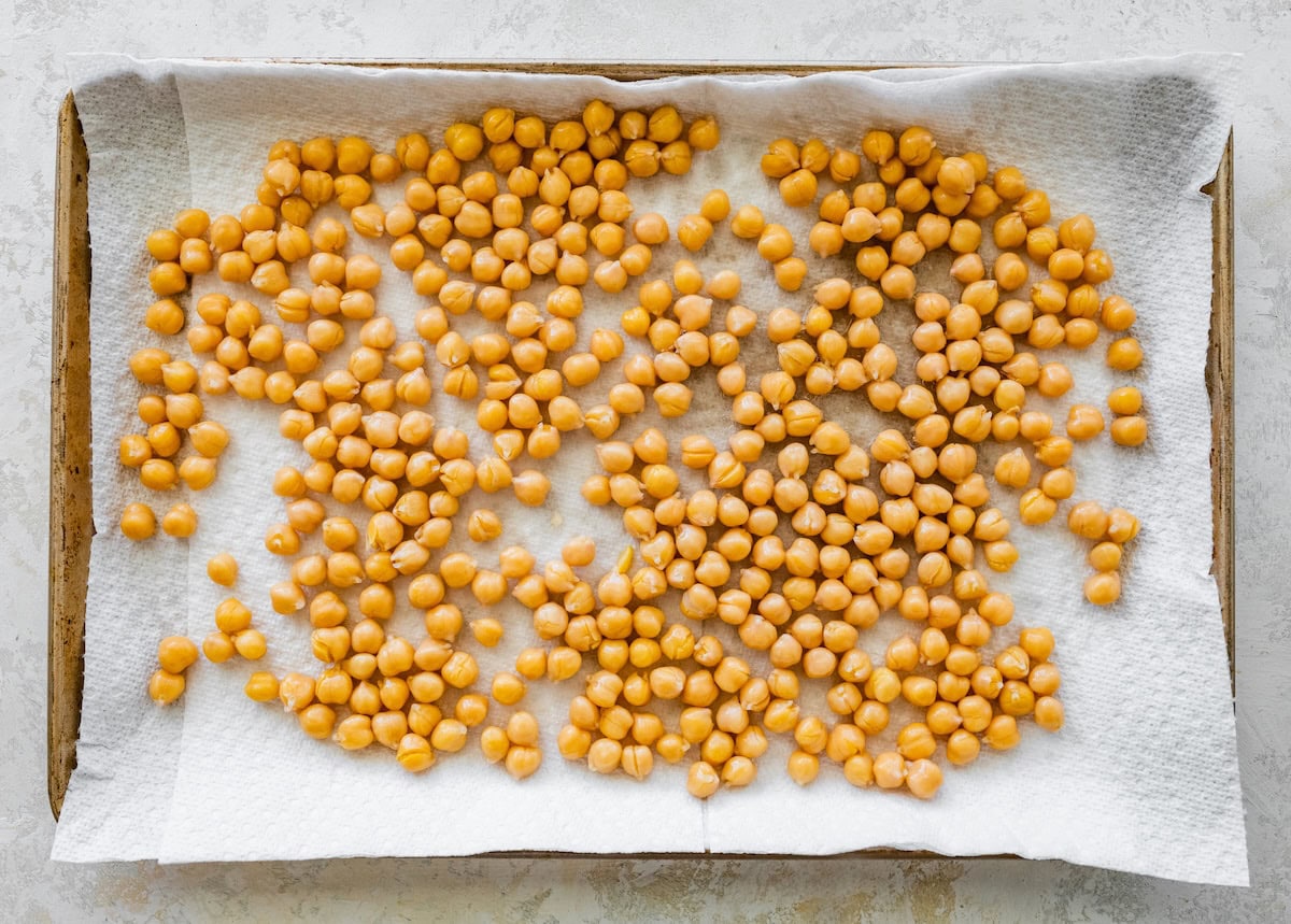 Rinsed chickpeas drying on a baking sheet lined with paper towels.