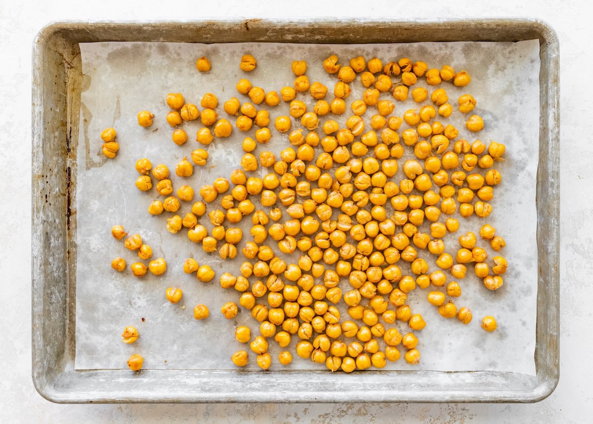 Partially roasted chickpeas baking on a parchment-lined sheet pan.