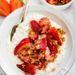Cottage cheese in a bowl topped with roasted strawberries, rolled oats and coconut. There is a silver spoon in the bowl.