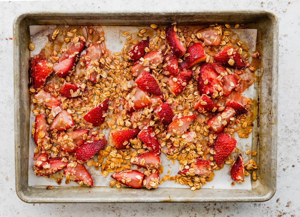 Roasted strawberries with oats and coconut on a parchment-lined baking sheet.