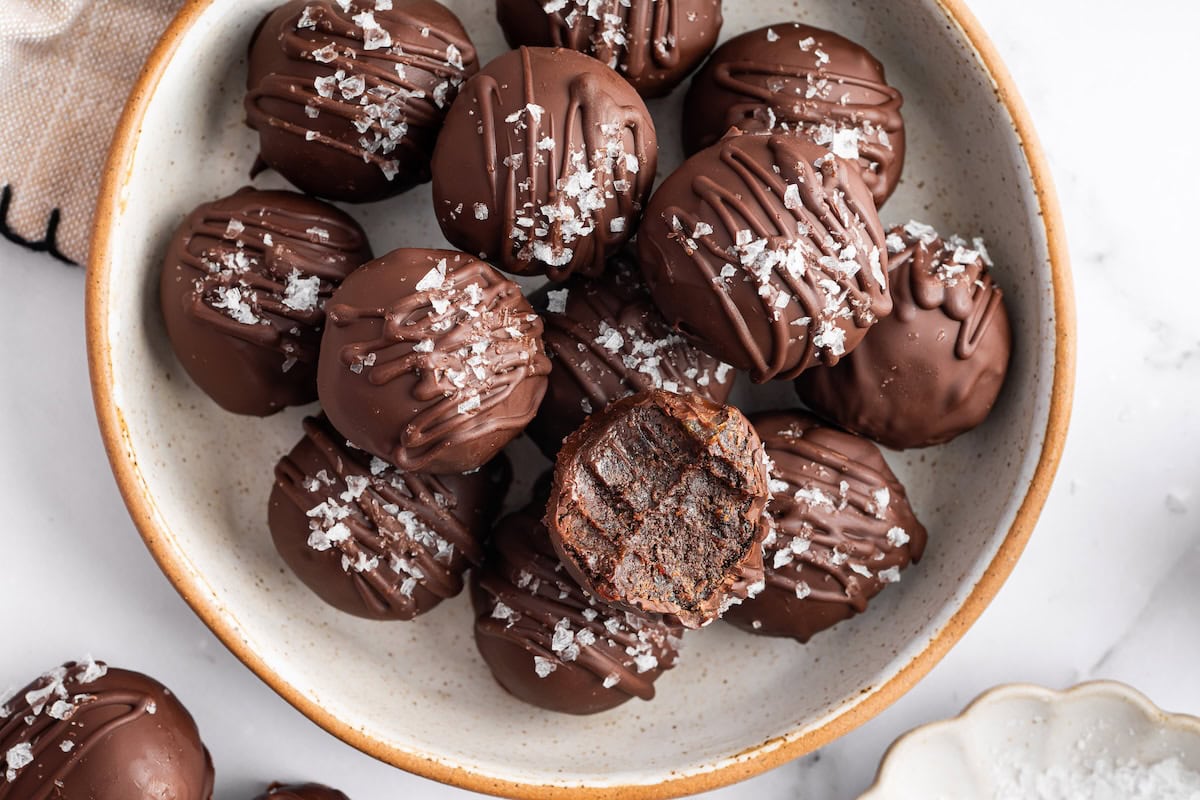 Bowl of chocolate protein balls stacked with flaky sea salt on top and one bitten into.