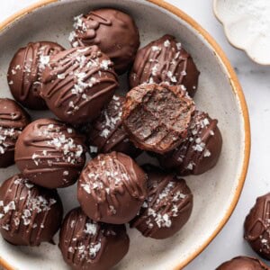 Bowl of chocolate protein balls stacked with flaky sea salt on top and one bitten into.