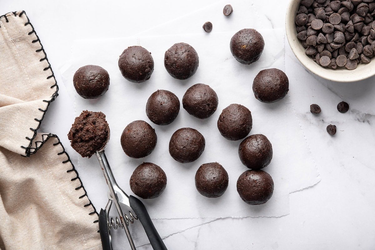 Scooped protein ball mixture portioned on parchment paper with a cookie scoop.