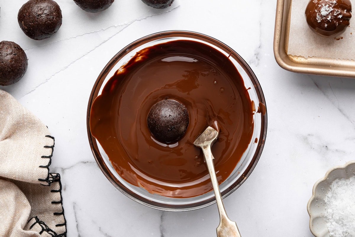 Protein ball being dipped into melted chocolate with a spoon.