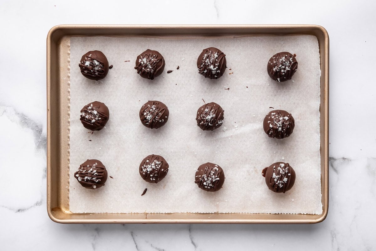 12 salted chocolate protein balls on a baking tray lined with parchment paper, pre-dipped stage.