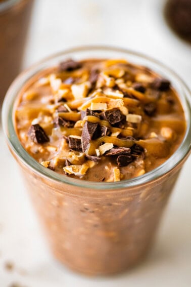 One glass jar filled with samoas overnight oats. It's topped with chocolate chunks, date caramel and toasted coconut.