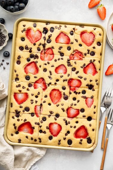 Sheet pan pancakes topped with strawberries and chocolate chips, freshly baked and cut into squares.