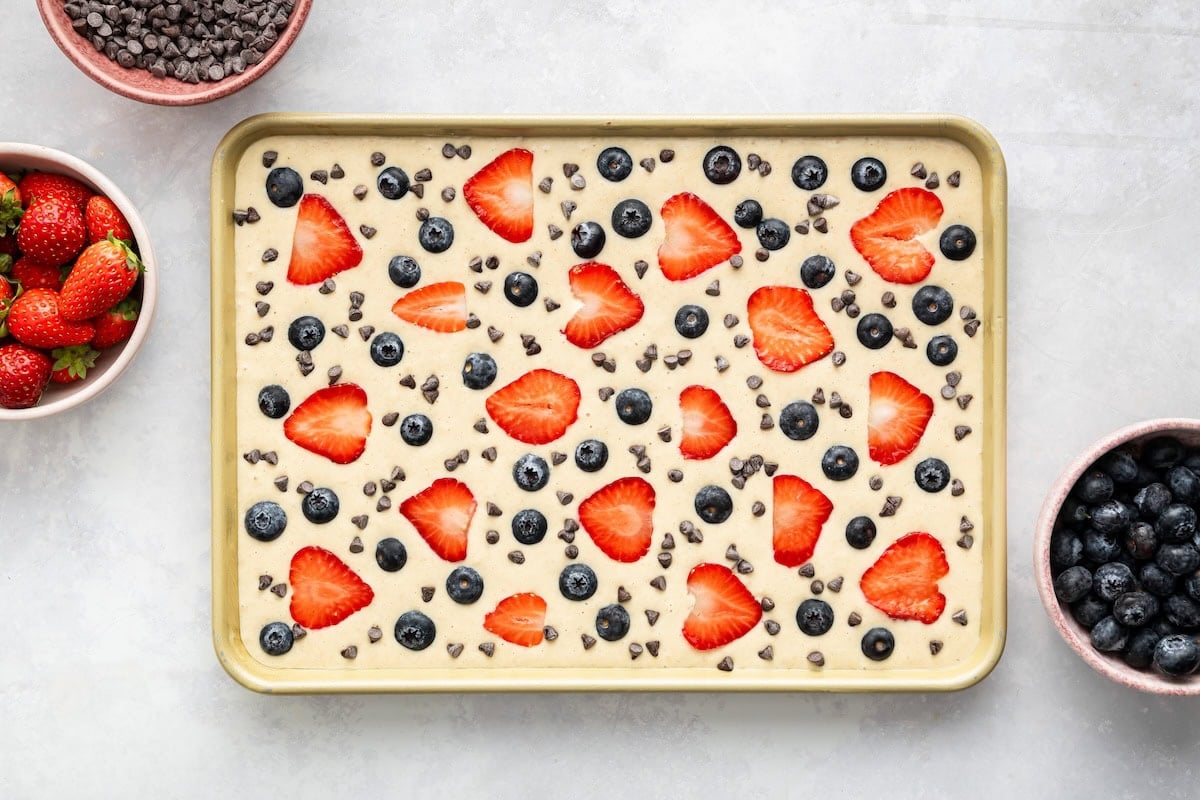 Quarter sheet pan filled with pancake batter and toppings ready to bake.