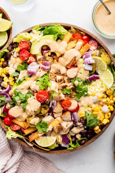 A southwest chicken salad in a large wooden bowl topped with a creamy southwest dressing.
