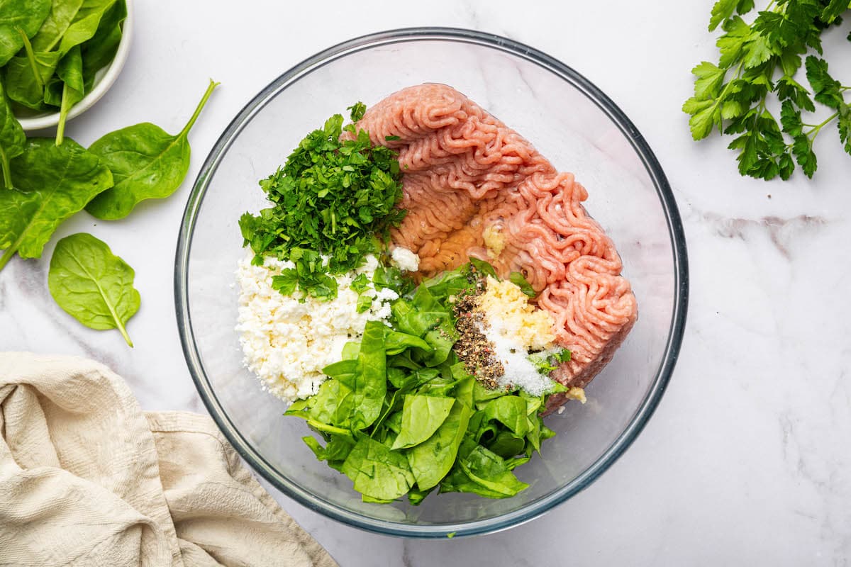 The spinach feta turkey burger ingredients in a glass mixing bowl: ground turkey, spinach, feta, parsley, salt, pepper, garlic and egg whites.