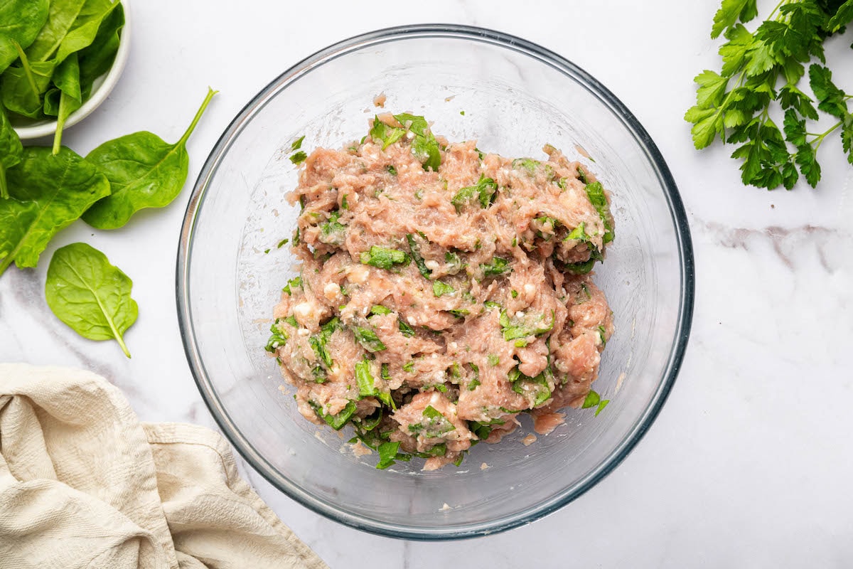 The spinach feta turkey burger mixture combined in a glass mixing bowl.
