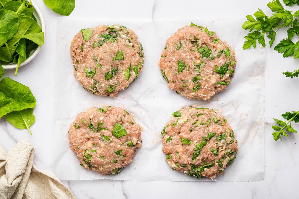Four raw spinach feta turkey burger patties formed and spread out on parchment paper.