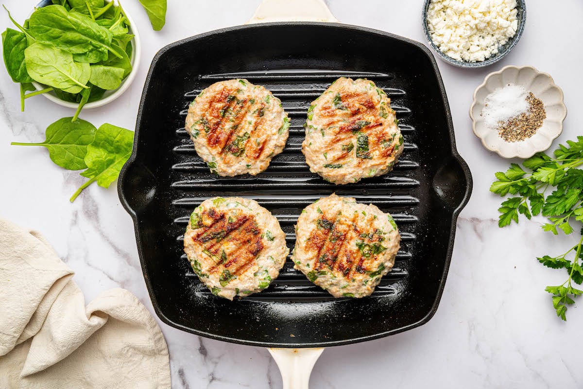 Four cooked spinach feta turkey burgers on a grill top.