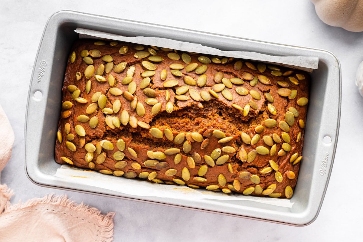 Homemade Starbucks pumpkin bread cooling in a loaf pan with pepitas on top.