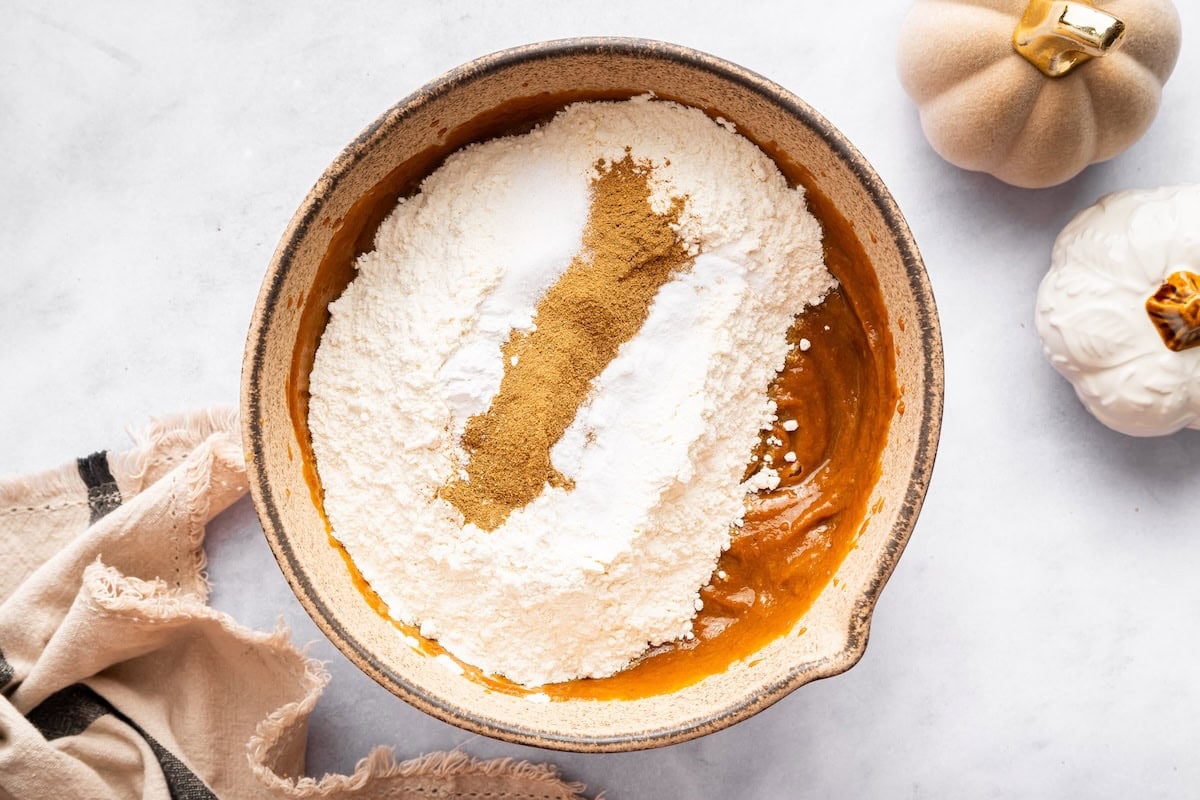 Dry ingredients added on top of wet pumpkin mixture in a mixing bowl.