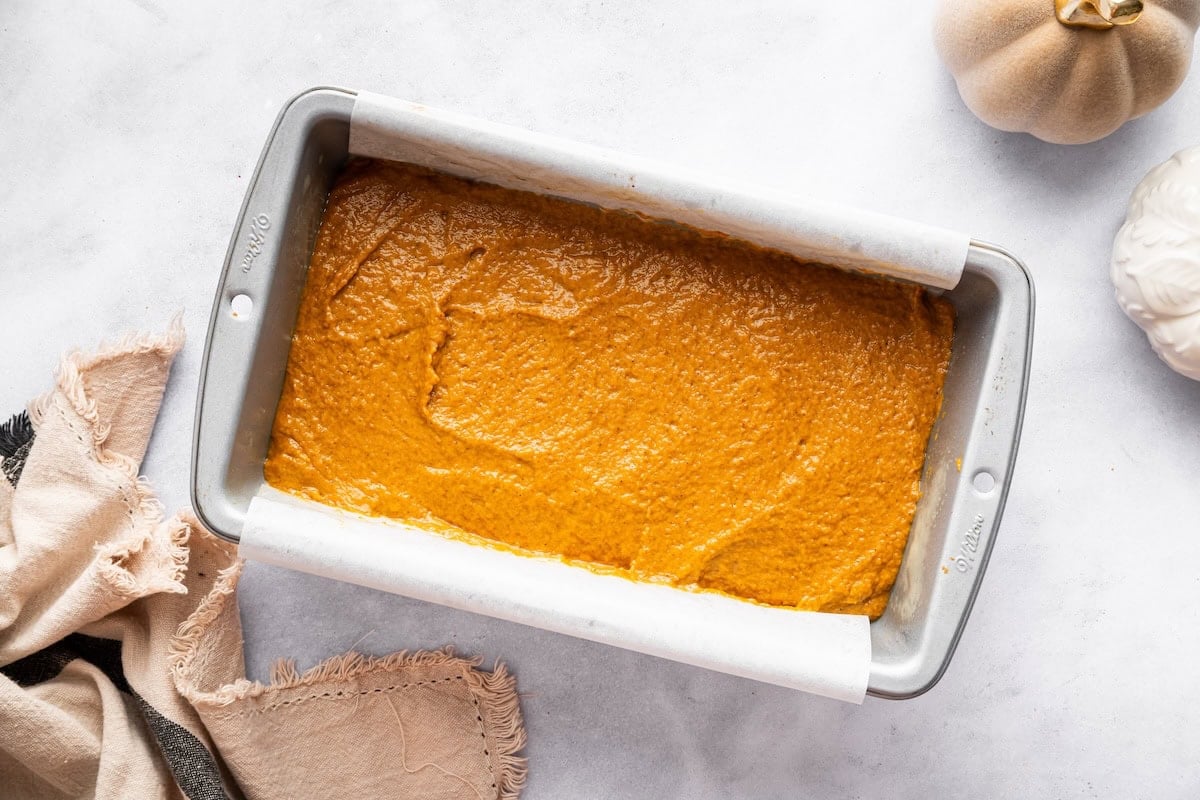 Pumpkin batter spread evenly in a greased loaf pan before baking.