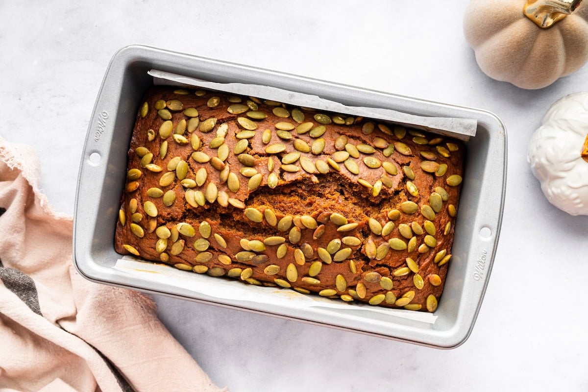 Freshly baked Starbucks pumpkin bread in a loaf pan topped with pepitas.