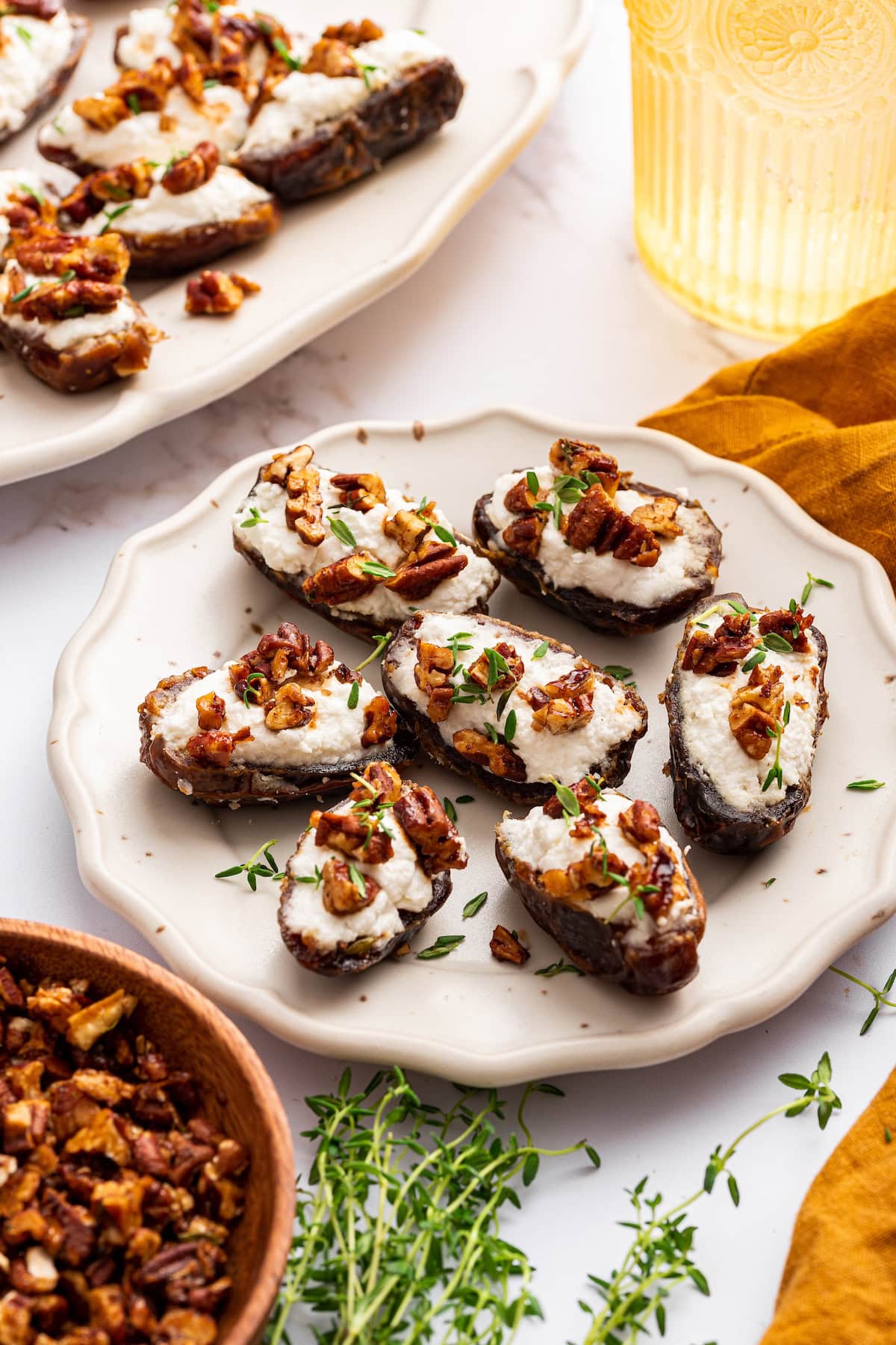 A small plate of multiple dates that are stuffed with goat cheese and topped with chopped pecans and fresh thyme.