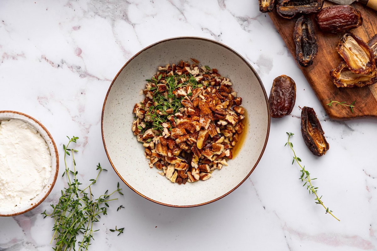 A bowl of maple syrup with chopped pecans and fresh thyme.