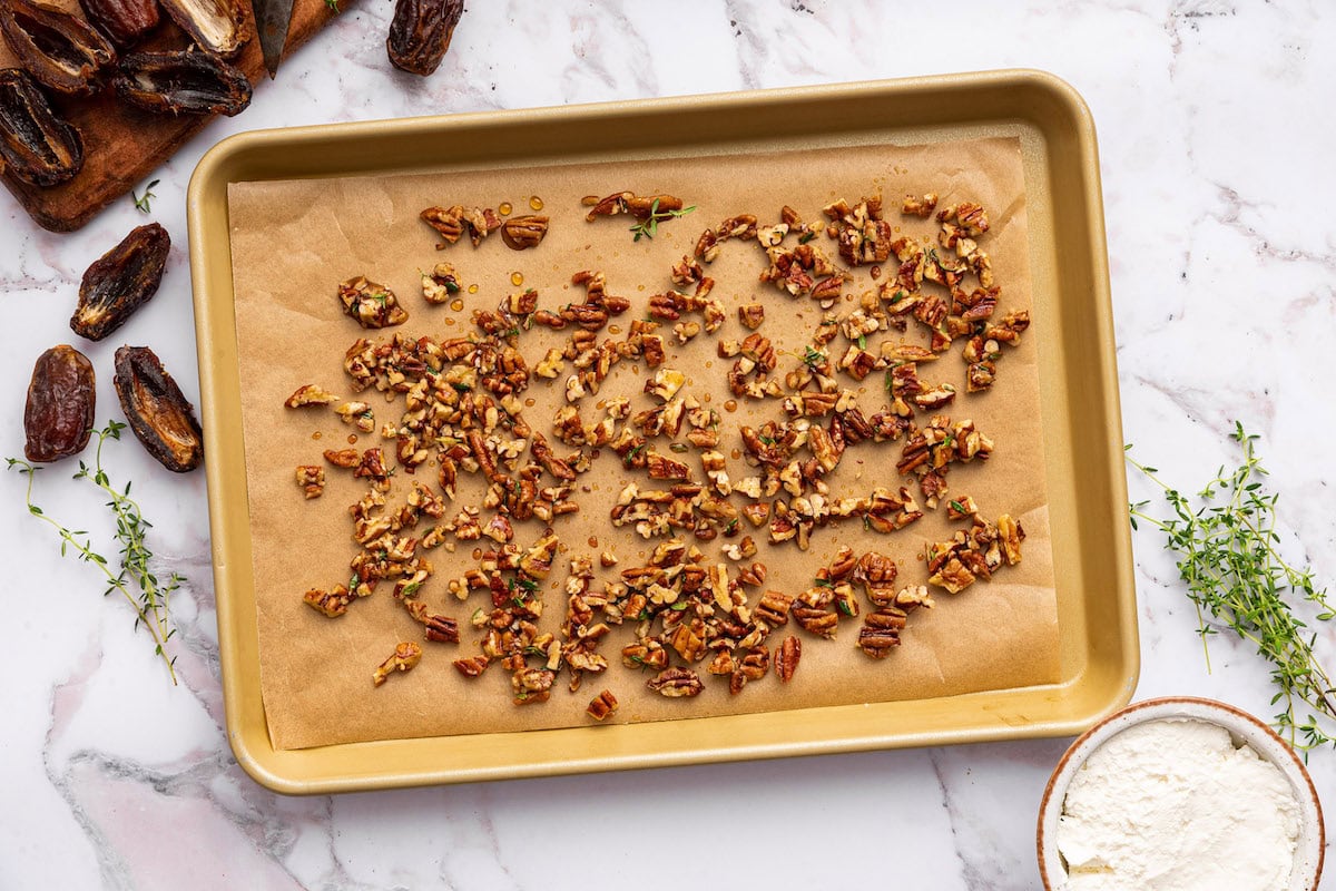 Chopped pecans with maple syrup and fresh thyme on a baking tray.