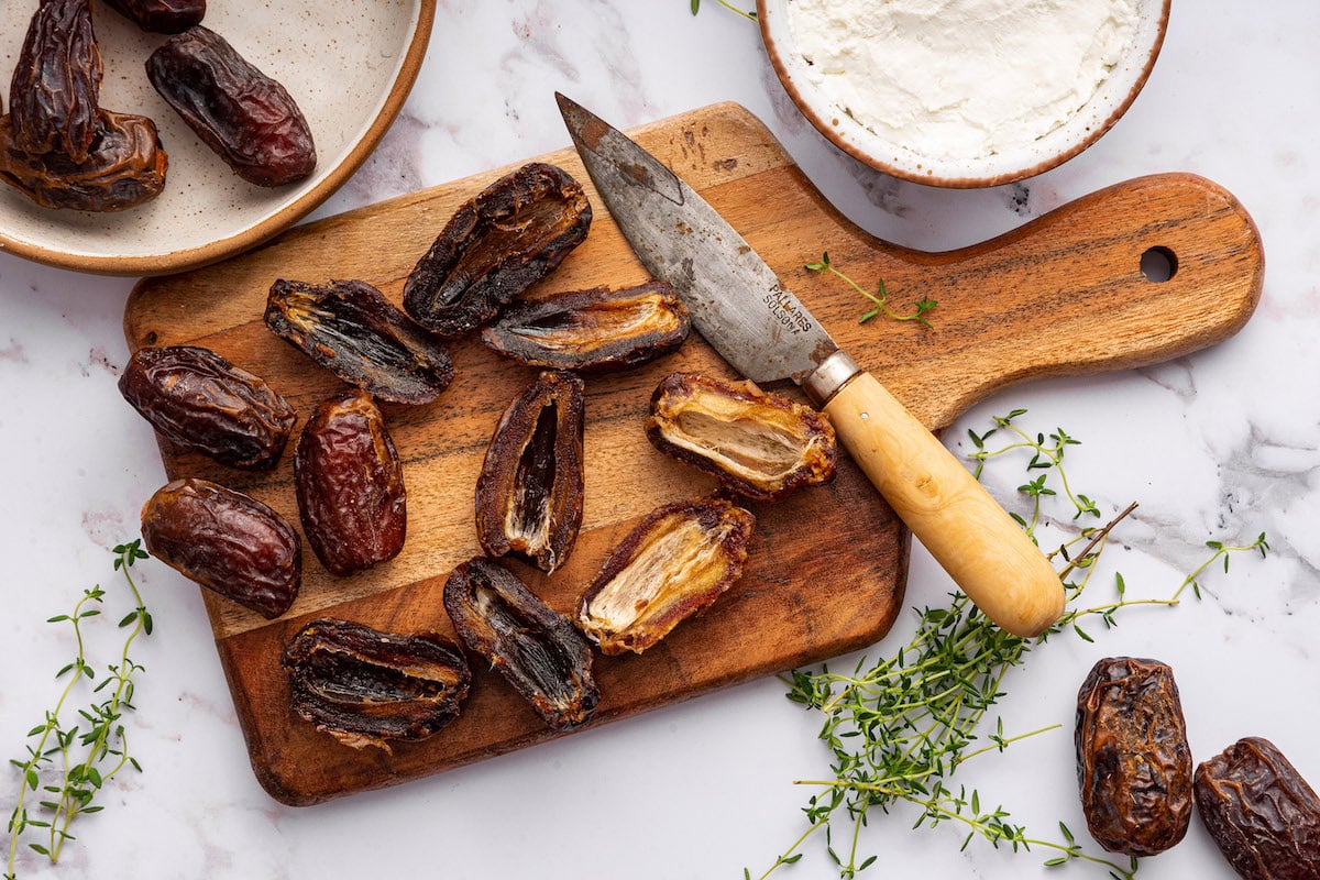 A wooden cutting board with a knife and multiple dates cut in half.
