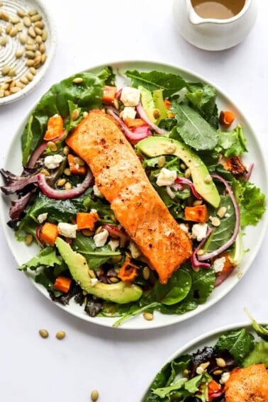 A plate of superfood salad topped with a filet of salmon topped with quick pickled onions, sweet potato croutons and a lemon vinaigrette.