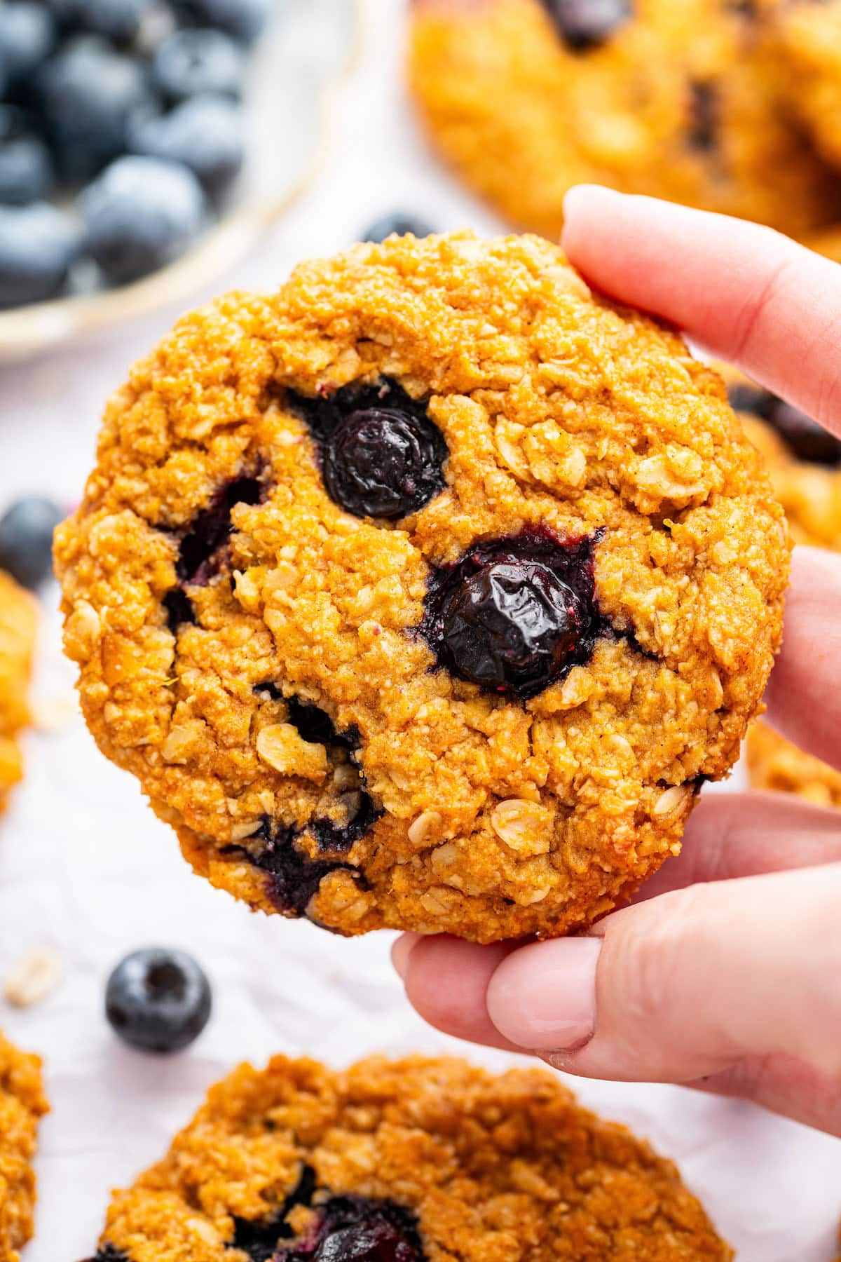 A woman's hand holding a sweet potato blueberry oatmeal cookie.