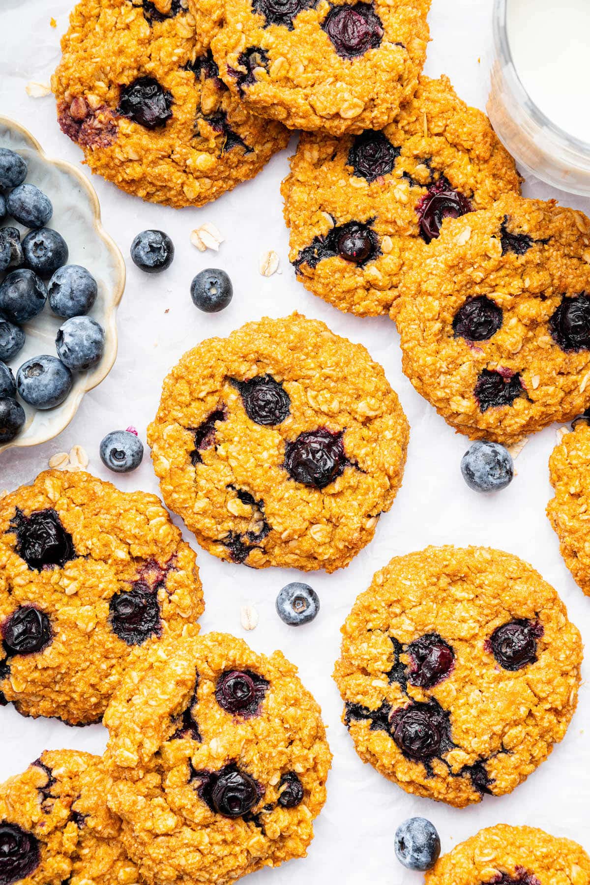 12 sweet potato blueberry oatmeal cookies spread out on a counter top. Fresh blueberries are scattered next to the cookies.