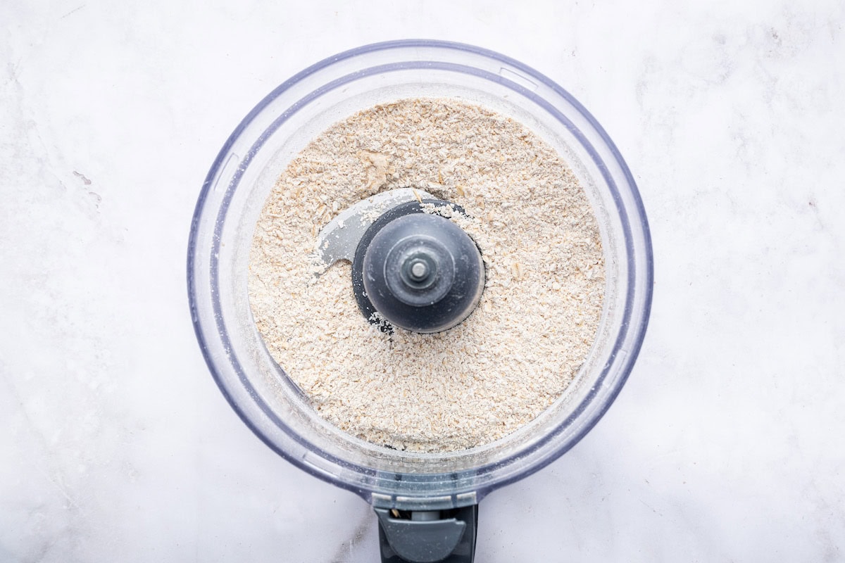 Rolled oats blended into oat flour in the bowl of a food processor.